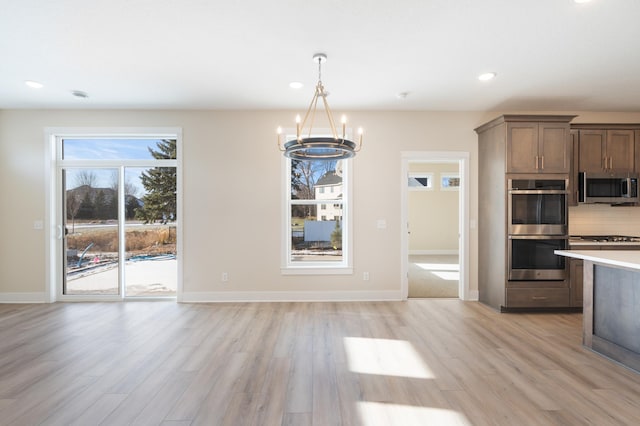 kitchen featuring appliances with stainless steel finishes, an inviting chandelier, light countertops, light wood-type flooring, and backsplash