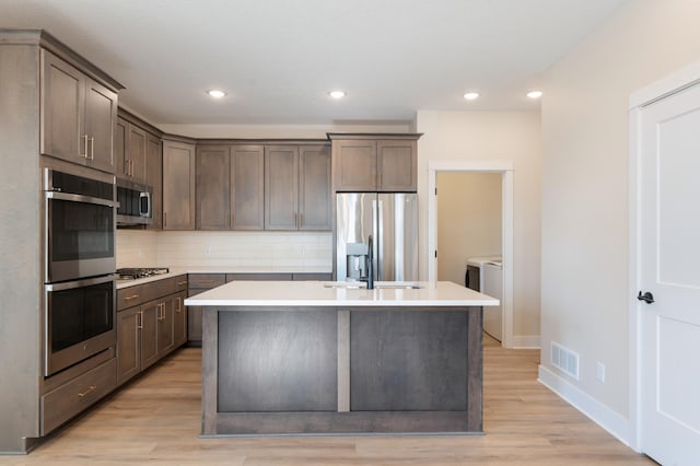 kitchen featuring separate washer and dryer, visible vents, appliances with stainless steel finishes, decorative backsplash, and a center island with sink