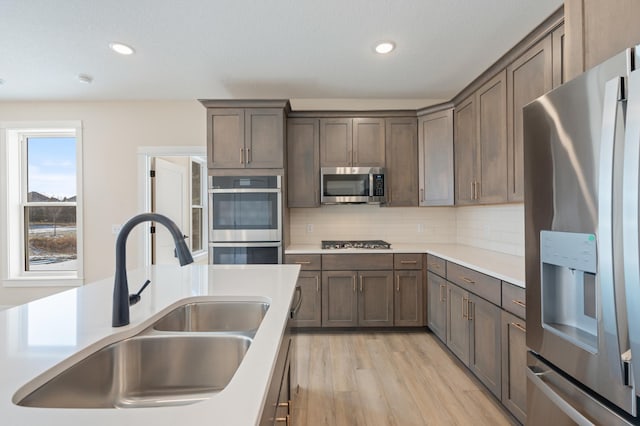 kitchen with a sink, light countertops, appliances with stainless steel finishes, light wood-type flooring, and backsplash