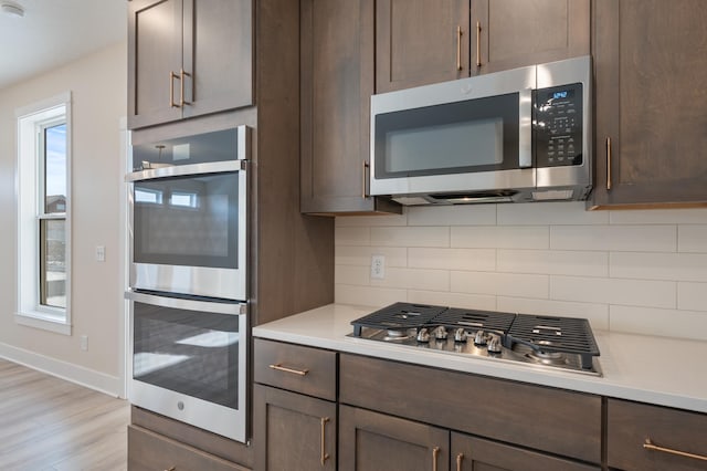 kitchen featuring tasteful backsplash, light countertops, light wood-style flooring, appliances with stainless steel finishes, and dark brown cabinetry