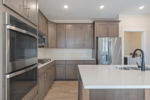 kitchen with appliances with stainless steel finishes, light wood-type flooring, a sink, and decorative backsplash