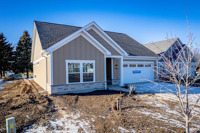 view of front of home with an attached garage, stone siding, a shingled roof, and board and batten siding