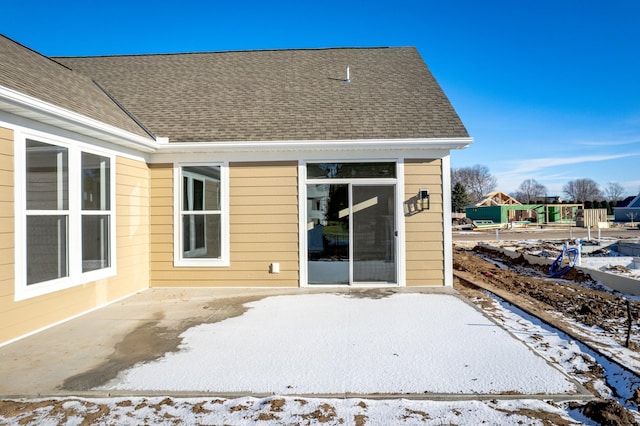 snow covered property with a shingled roof and a patio