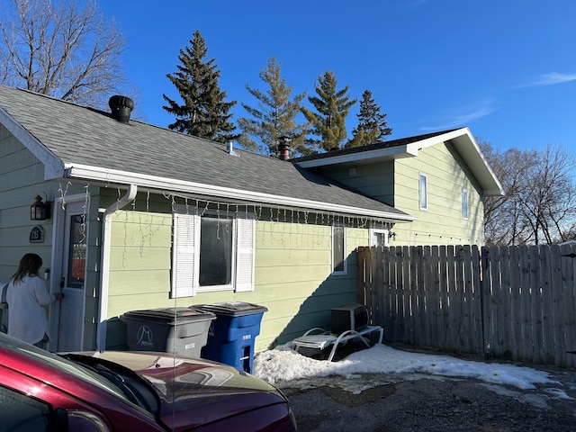 view of home's exterior featuring fence and a shingled roof