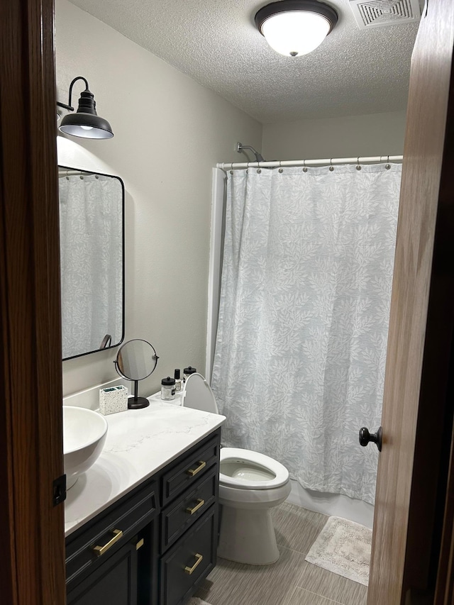 full bathroom featuring tile patterned floors, visible vents, toilet, vanity, and a textured ceiling
