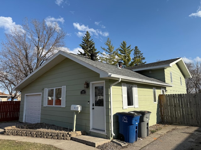 view of front of home with fence, roof with shingles, and a garage