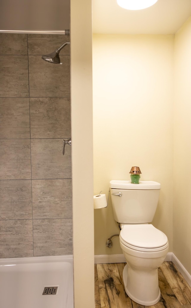 full bathroom featuring tiled shower, wood finished floors, toilet, and baseboards