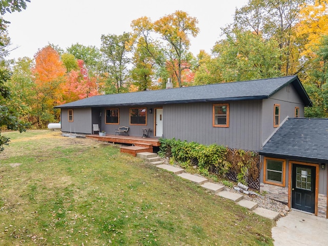 view of front of property with a chimney, a shingled roof, a deck, stone siding, and a front lawn