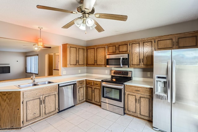 kitchen with stainless steel appliances, a peninsula, a sink, light countertops, and brown cabinetry