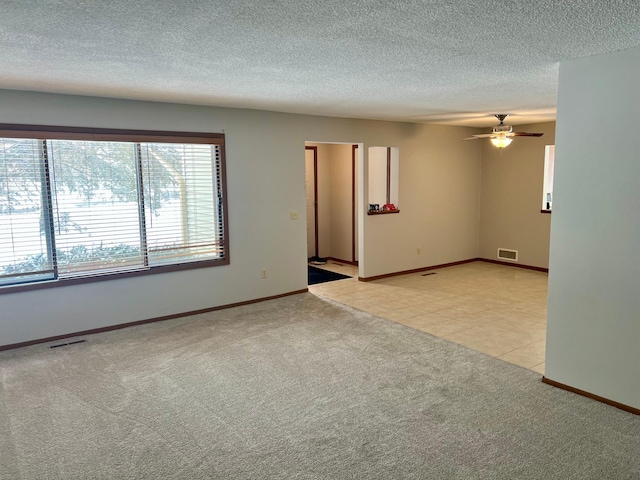 unfurnished room featuring light tile patterned floors, a textured ceiling, visible vents, and light colored carpet