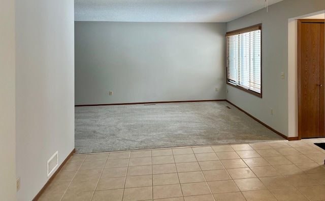 spare room featuring light carpet, light tile patterned floors, visible vents, and baseboards