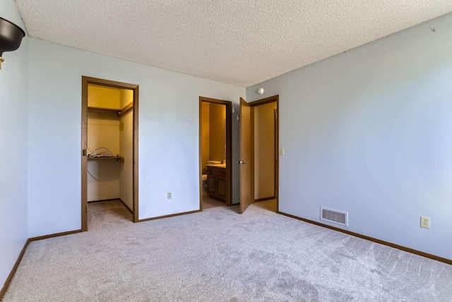 unfurnished bedroom with a textured ceiling, carpet flooring, visible vents, baseboards, and a spacious closet