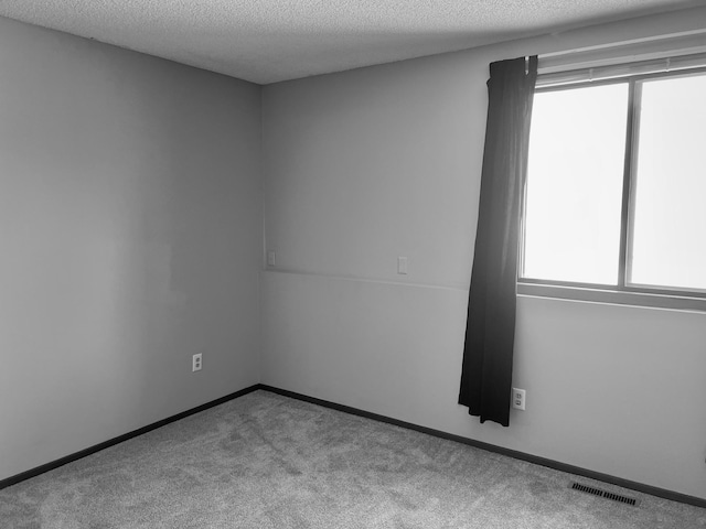 carpeted empty room with visible vents, a textured ceiling, and baseboards