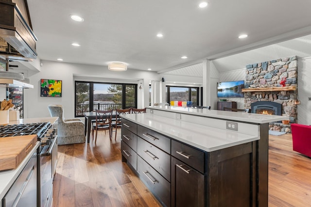 kitchen featuring stainless steel gas stove, dark brown cabinetry, open floor plan, wood finished floors, and light countertops