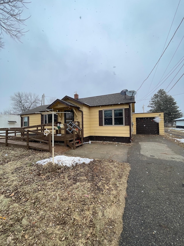 view of front of property featuring a garage, a chimney, a deck, and an outbuilding