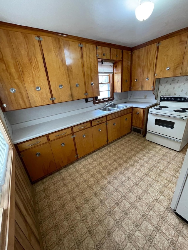 kitchen featuring brown cabinetry, white range with electric stovetop, light countertops, and a sink