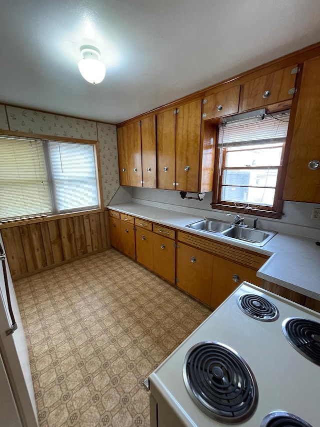 kitchen featuring brown cabinetry, white range with electric cooktop, a sink, and wallpapered walls