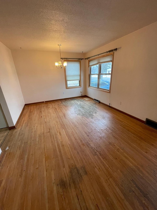 empty room featuring a chandelier, visible vents, a textured ceiling, and hardwood / wood-style flooring