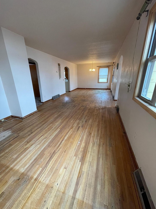 unfurnished living room with a wealth of natural light, arched walkways, visible vents, and hardwood / wood-style flooring