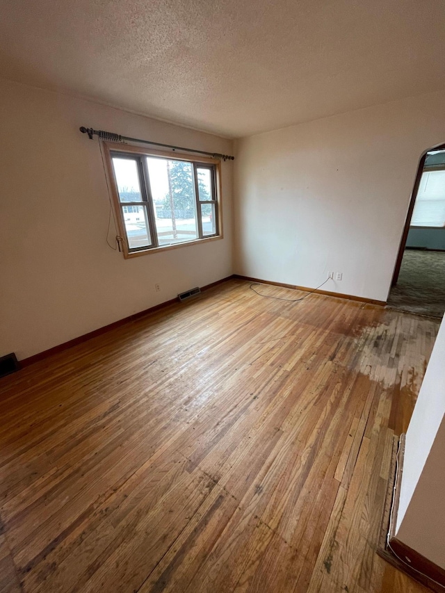 empty room featuring baseboards, a textured ceiling, visible vents, and hardwood / wood-style floors