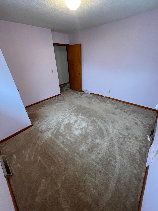 spare room with carpet flooring, visible vents, a textured ceiling, and baseboards