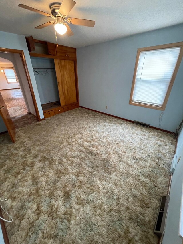 unfurnished bedroom featuring a textured ceiling, ceiling fan, carpet floors, visible vents, and a closet