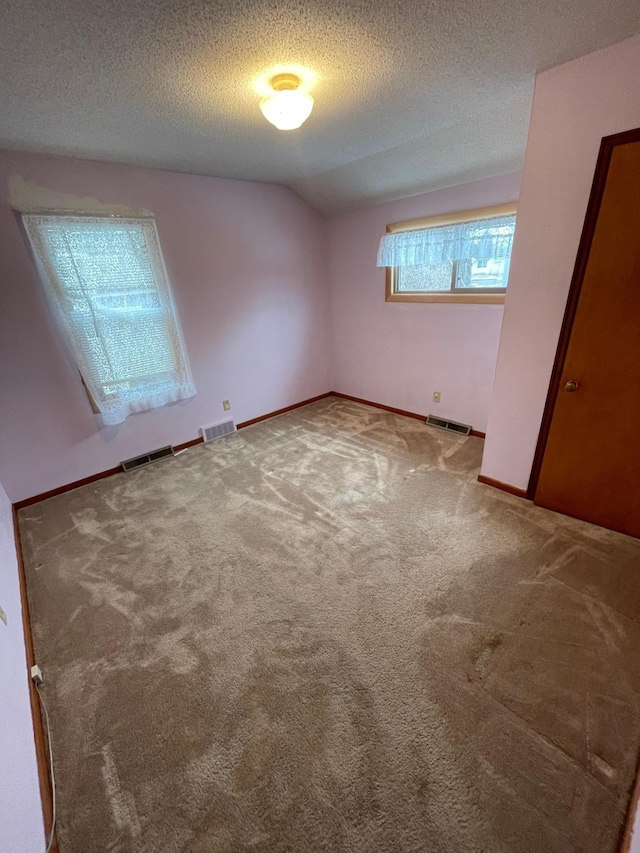 unfurnished bedroom with lofted ceiling, visible vents, a textured ceiling, and carpet flooring