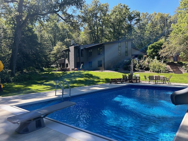 outdoor pool with a diving board, a yard, a water slide, and a patio area