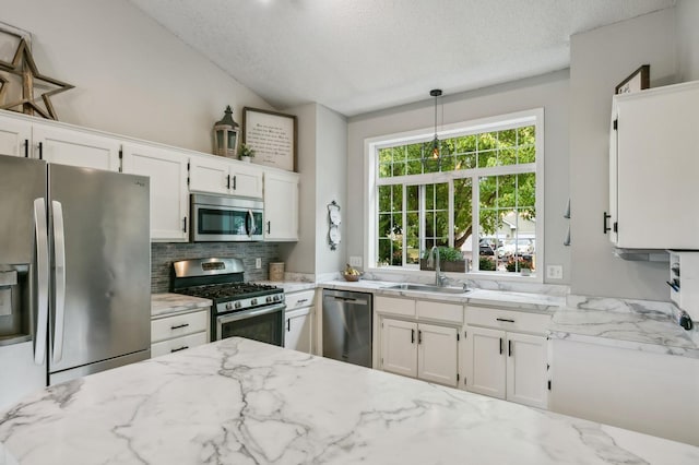 kitchen with appliances with stainless steel finishes, white cabinets, a sink, and light stone countertops