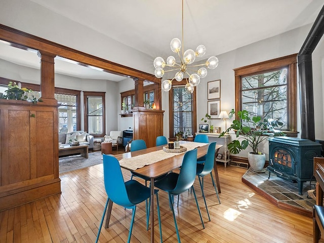 dining space with a wealth of natural light, ornate columns, a wood stove, and light wood-style floors