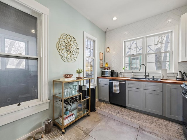 kitchen with backsplash, butcher block counters, dishwashing machine, gray cabinets, and a sink