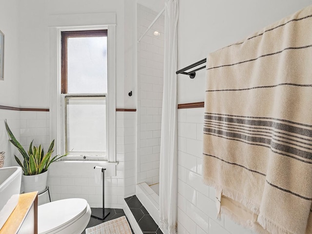 bathroom featuring tile patterned flooring, toilet, a tile shower, wainscoting, and tile walls