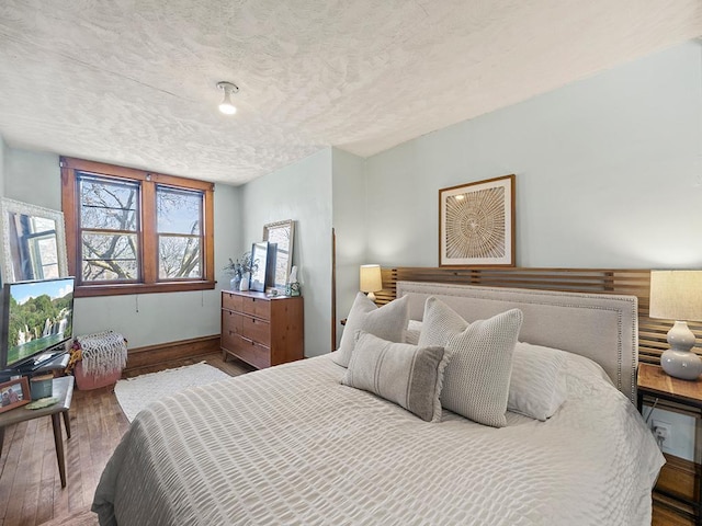 bedroom with wood finished floors, baseboards, and a textured ceiling