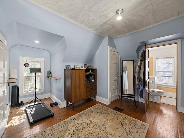 workout area with baseboards, hardwood / wood-style floors, and vaulted ceiling