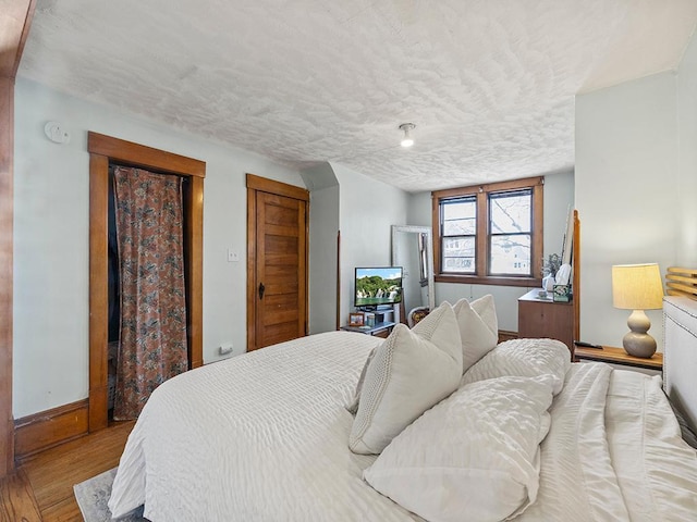 bedroom with baseboards, a textured ceiling, and wood finished floors