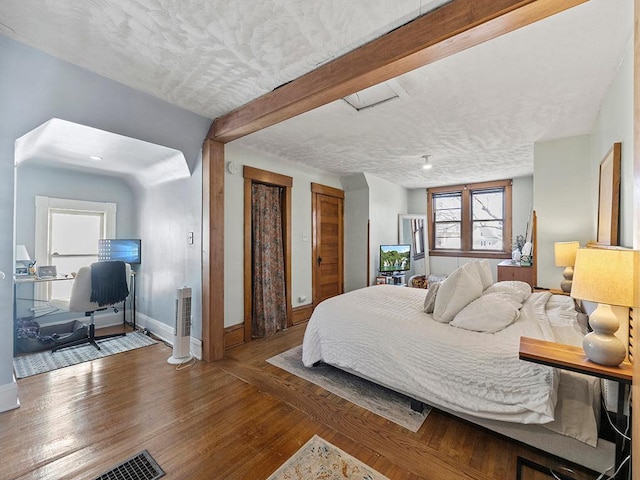 bedroom featuring beam ceiling, two closets, a textured ceiling, wood finished floors, and baseboards