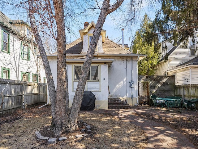 rear view of property with stucco siding, a shingled roof, a chimney, and fence