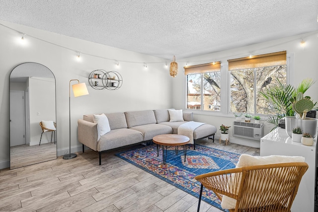 living room with track lighting, light wood-style flooring, a wall unit AC, and a textured ceiling