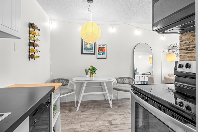 kitchen with wood finish floors, a textured ceiling, stainless steel range with electric cooktop, baseboards, and hanging light fixtures