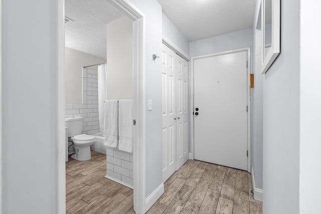 hall featuring wainscoting, a textured ceiling, tile walls, and wood tiled floor