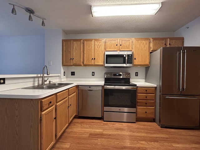 kitchen with appliances with stainless steel finishes, a peninsula, light countertops, light wood-style floors, and a sink