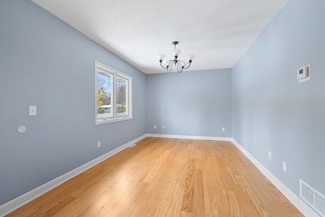 unfurnished room featuring a chandelier, a textured ceiling, visible vents, light wood-style floors, and baseboards