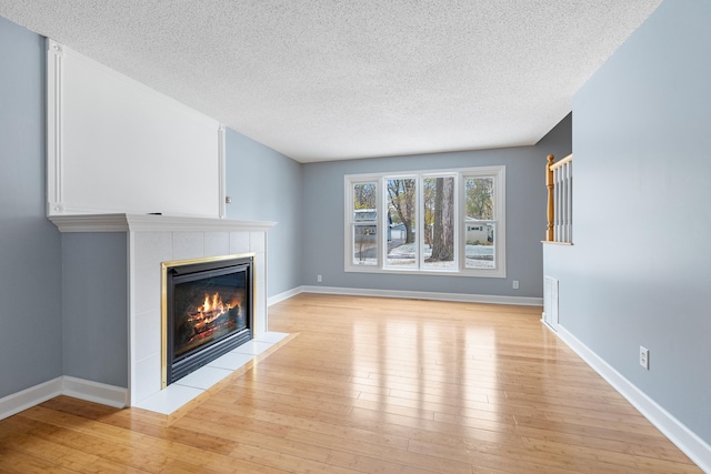 unfurnished living room with light wood-style floors, a textured ceiling, baseboards, and a tiled fireplace