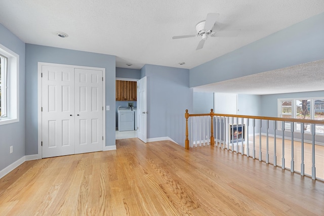 unfurnished room featuring a textured ceiling, ceiling fan, washing machine and dryer, baseboards, and light wood-style floors