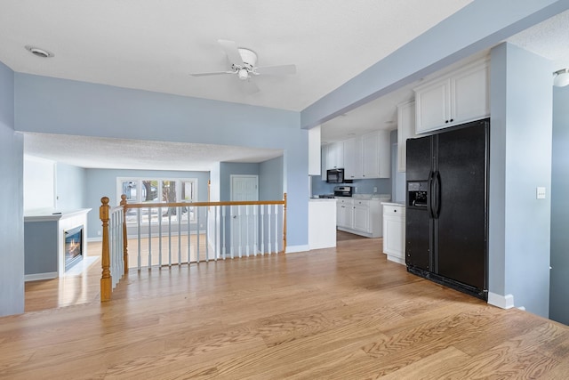 kitchen featuring light wood finished floors, baseboards, white cabinets, a glass covered fireplace, and black appliances