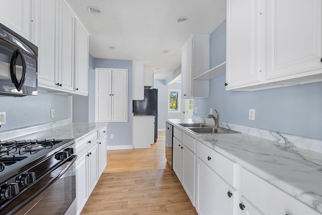 kitchen with black appliances, a sink, light wood-style flooring, and white cabinets