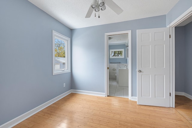 unfurnished bedroom with light wood-style flooring, a ceiling fan, connected bathroom, a textured ceiling, and baseboards