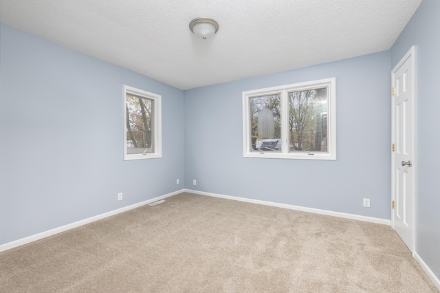 carpeted spare room featuring a textured ceiling, visible vents, and baseboards