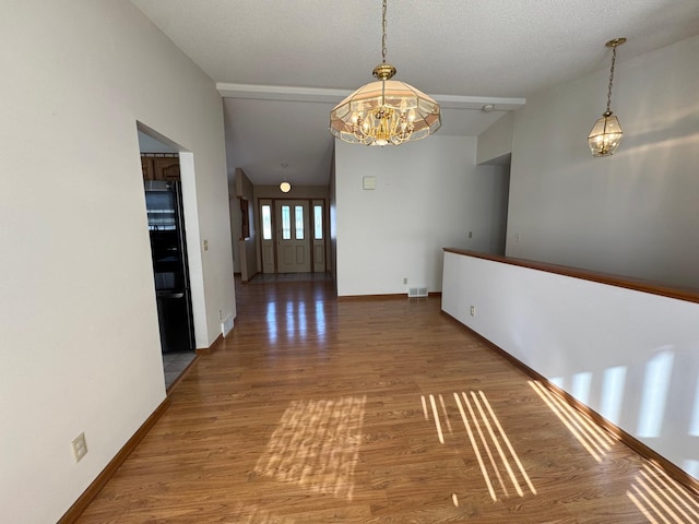 hallway with visible vents, a notable chandelier, baseboards, and wood finished floors