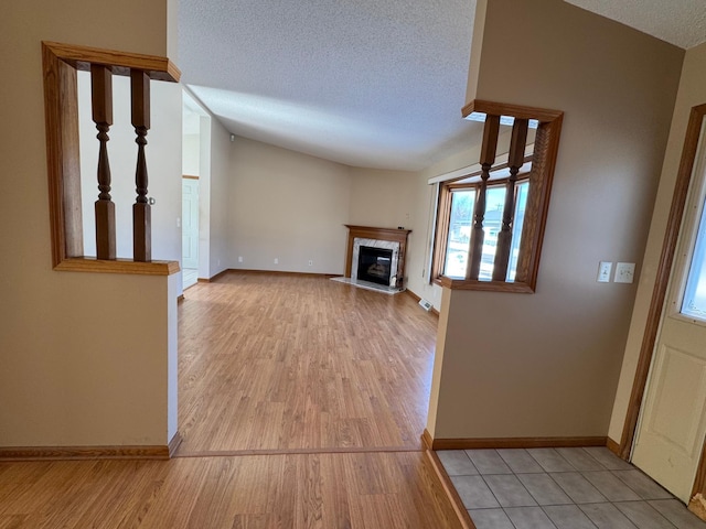 unfurnished living room with a textured ceiling, light wood finished floors, a fireplace, and baseboards